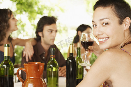 背景中与朋友一起享用红酒的快乐年轻女性的画像