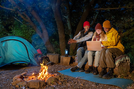 快乐的多民族朋友玩音乐，晚上在大自然中享受篝火露营