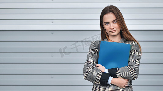一个年轻的女学生，在条纹墙上有一个蓝色文件夹。