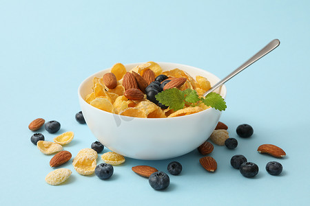 金色奶罐主图摄影照片_蓝色背景中带麦片、杏仁、薄荷和蓝莓的碗