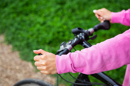 一个穿着粉色运动衫的女孩抓着自行车的车把，在公园里骑自行车。