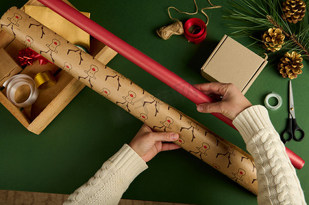 端午节礼摄影照片_女人的手拿着礼品纸，在绿色背景下选择包装圣诞或新年礼物的包装材料