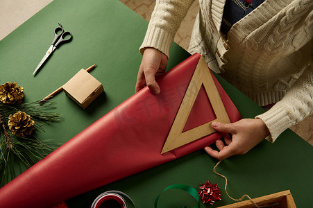 顶视图女人的手用木尺，测量包装圣诞礼物的红色包装纸的数量。