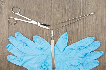 手术刀摄影照片_木质背景上带手套的银色手术刀外科剪刀和镊子