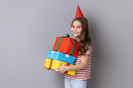 小女孩穿着 T 恤和派对锥，拥抱一堆礼物，庆祝生日。