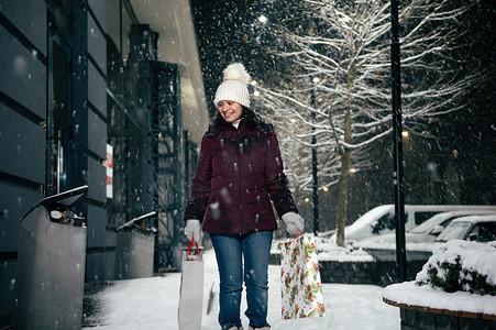 令人愉快的年轻女子走在街上，手里拿着购物袋，手里拿着圣诞礼品盒。