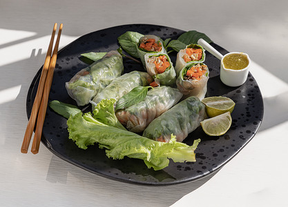 健康的越南春卷作为蔬菜的一部分，配上辣酱和黑色陶瓷盘上的木筷子。