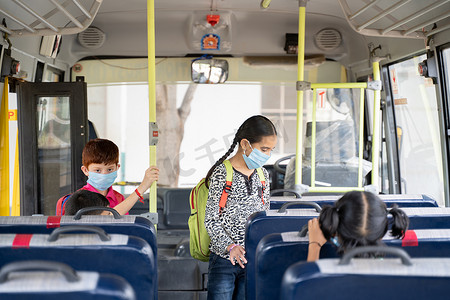 戴着医用口罩的孩子进入校车并坐在座位上，同时由于冠状病毒或 covid-19 大流行病而保持社交距离 — 学校重新开放或返校的概念