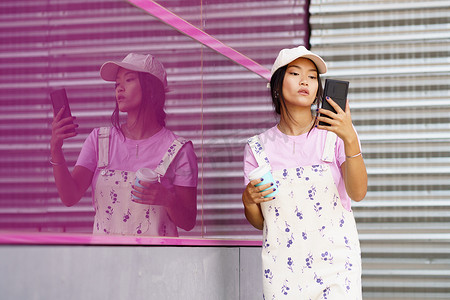 粉色墙壁摄影照片_粉色墙壁附近有智能手机和咖啡的年轻亚洲女性