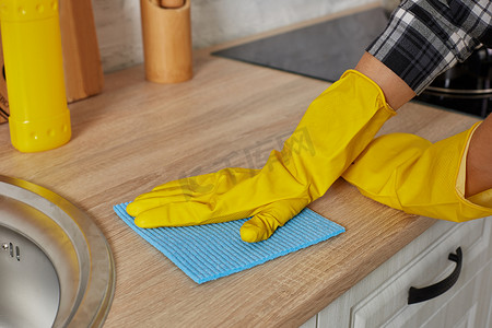 正在清洁摄影照片_戴着绿色抹布手套的手正在清洁厨柜 — 家务和家政概念