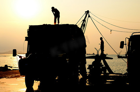 日落大海摄影照片_日落天空卡车上人的轮廓，工人为渔船破冰