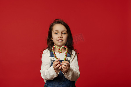 长头发的漂亮小女孩拿着心形条纹糖果，突显在红色背景中