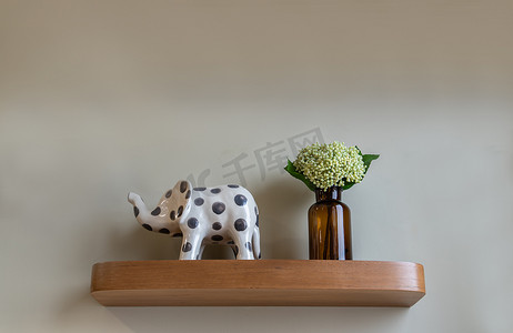 大象木摄影照片_棕色玻璃瓶中的绿色花朵和客厅木架上大象形状的陶瓷花束。