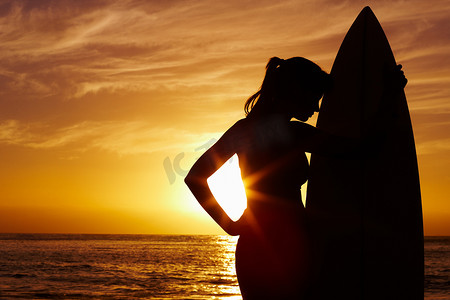 冲浪海上摄影照片_现出轮廓的女人与冲浪板反对海上风景秀丽的日落。