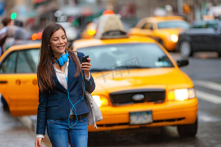 请按时下班摄影照片_在纽约市行走的年轻女性使用电话应用程序乘坐出租车，戴着耳机下班通勤。