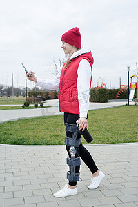 腿部手术后佩戴护膝或矫形器的女性使用智能手机在公园行走