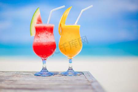 黄色西瓜摄影照片_令人惊叹的绿松石海背景中的两杯西瓜和芒果鸡尾酒