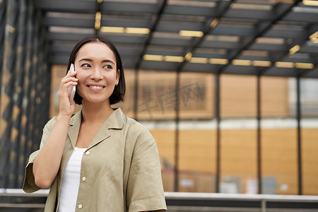 快乐的亚洲女人站在城市的公交车站上，用手机聊天。