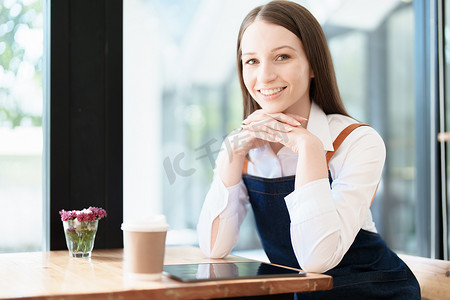 克蓝英蓝笑脸摄影照片_开始并开设一家小企业，一位年轻的亚洲女性围着围裙站在咖啡店吧台前露出笑脸。