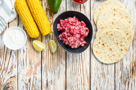 用切碎的有机肉、玉米、卡尔萨在白色纹理木桌上烹制墨西哥炸玉米饼配料，顶视图有文字空间。