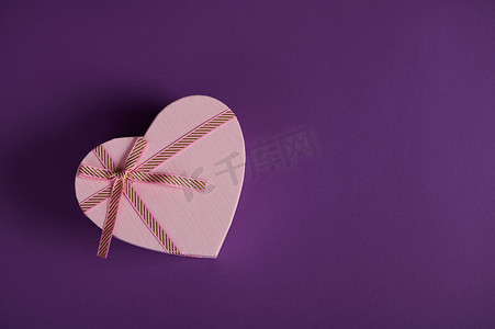 顶视图圣瓦伦丁节装饰心形礼盒，带粉色丝带蝴蝶结，突显在紫色背景中