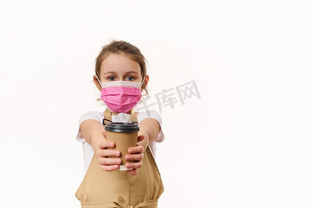 穿着厨师围裙和粉色医用安全面罩的可爱小女孩，在镜头前用纸杯分发外卖热饮