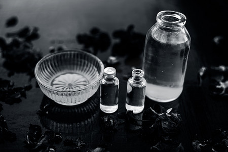 木质表面瓶子中的蓖麻油、茶树油和一些椰子油的特写，以及表面上还存在的一些生蜂蜜和玫瑰花瓣。