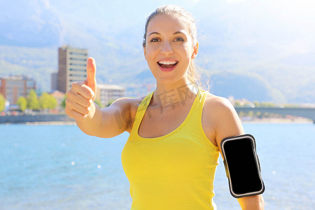 成功的女运动员在夏季跑步或户外运动前做积极的竖起大拇指手势并佩戴空白臂章进行广告宣传。