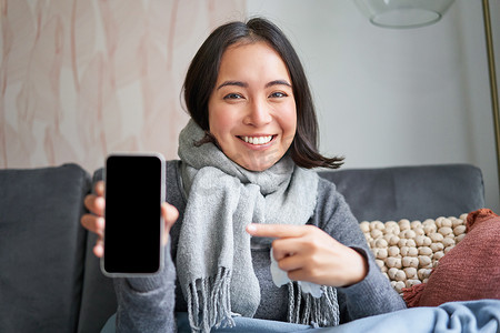 微笑女孩在家生病的画像，显示手机屏幕，推荐在线医疗应用、药房或智能手机上的 gp