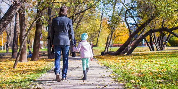 走在秋天公园的年轻父亲和小女孩背面图