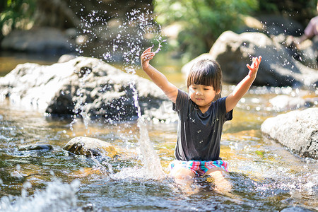 溪流玩耍摄影照片_小亚洲女孩在瀑布溪流中玩耍，溅起水花