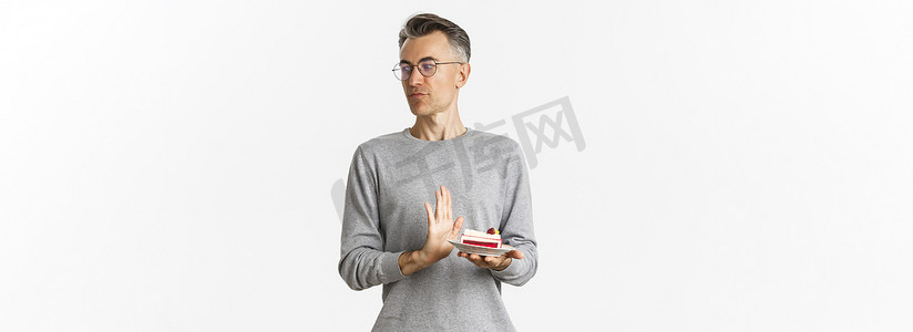 不悦的中年男子的画像，厌恶地看着别处，拒绝一块蛋糕，站在白色背景上烦恼