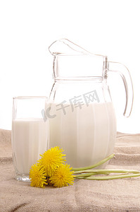 牛奶玻璃壶摄影照片_白色背景中带鲜奶和黄色花朵的玻璃壶