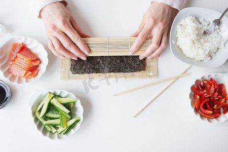 寿司准备过程中，女孩制作不同口味的寿司——新鲜三文鱼、鱼子酱、鳄梨、黄瓜、生姜、米饭。