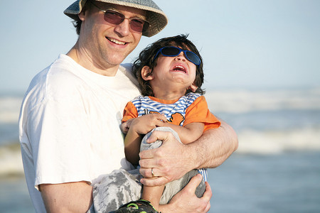 父亲在海滩上抱着哭泣的孩子