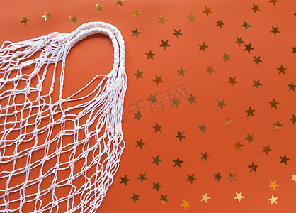 橙色星星摄影照片_橙色背景的白色绳子棉质生态袋，带有金色星星装饰。