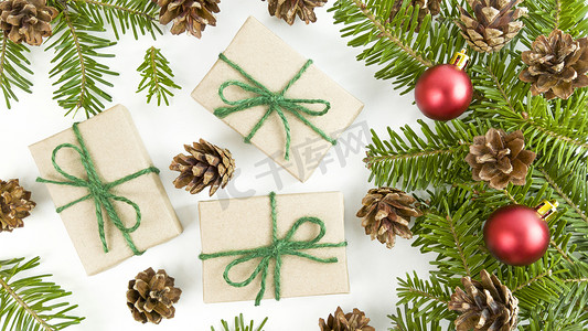 小新壁纸摄影照片_节日明信片上有工艺礼品盒、冷杉树枝、锥体和白色背景上的红色圣诞小饰品。