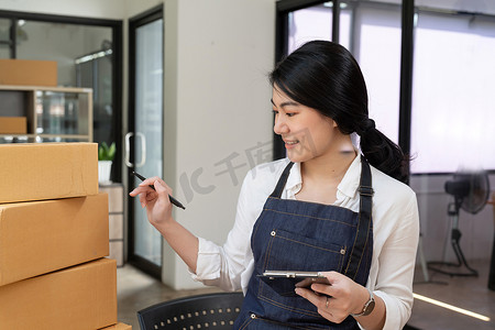 快乐的年轻亚洲女性创业小企业自由职业者，家里有包裹箱和笔记本电脑。