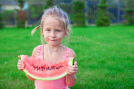 可爱的蹒跚学步的小孩坐在草地上拿着一块西瓜