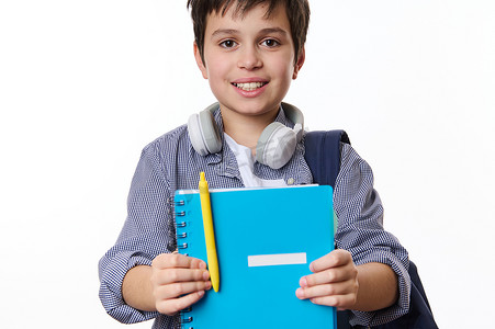 黄色青春摄影照片_聪明的男孩，小学生拿着蓝色的字帖和黄色的笔，微笑着看着镜头。