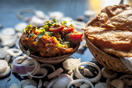 Batate ki sukhi bhaji 或土豆 sabji 在粘土碗中的特写镜头，以及一些干燥的普通油炸 puri 和一些黑色表面上的切洋葱。