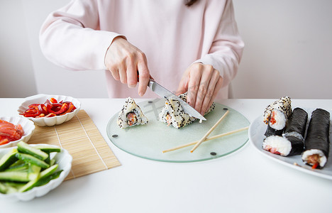 制作寿司的过程，女孩制作不同口味的寿司——新鲜的三文鱼、鱼子酱、牛油果、黄瓜、生姜、米饭。