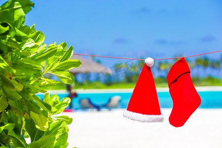 圣诞袜红色摄影照片_热带海滩上挂着红色圣诞帽和圣诞袜