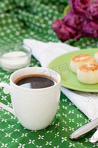 白色精致杯子里的黑咖啡，早餐用自制农夫奶酪制成的美味减肥芝士蛋糕，绿色桌布上的一束紫色郁金香。