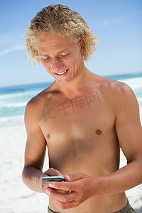 微笑的金发男子站在沙滩上发短信