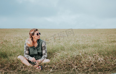 戴眼镜的女孩的画像盘腿坐在田里。