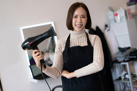 理发围裙摄影照片_手持合格理发工具的年轻亚洲女美发师的画像。