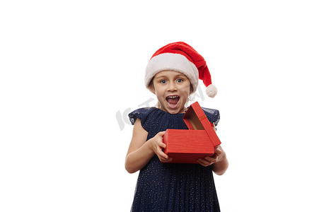戴着圣诞老人帽的快乐女婴，在打开快乐的圣诞礼物时表达幸福、快乐和惊喜