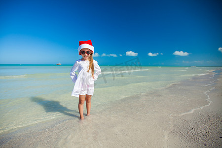 红色帽子圣诞老人和太阳镜的小女孩在海滩
