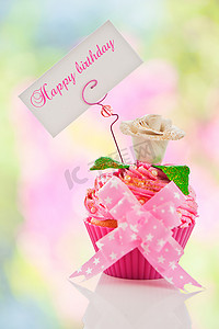 生日快乐庆祝蛋糕摄影照片_一个漂亮的粉色生日快乐纸杯蛋糕，上面有花和标签